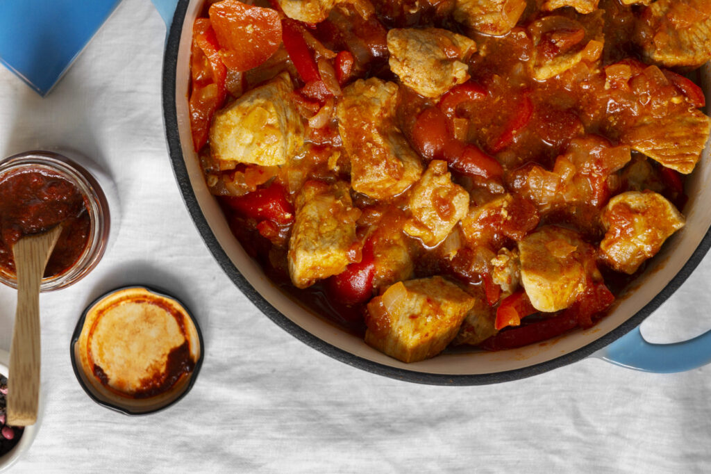 Cooked chicken being added to a pot of gumbo with rich broth and vegetables