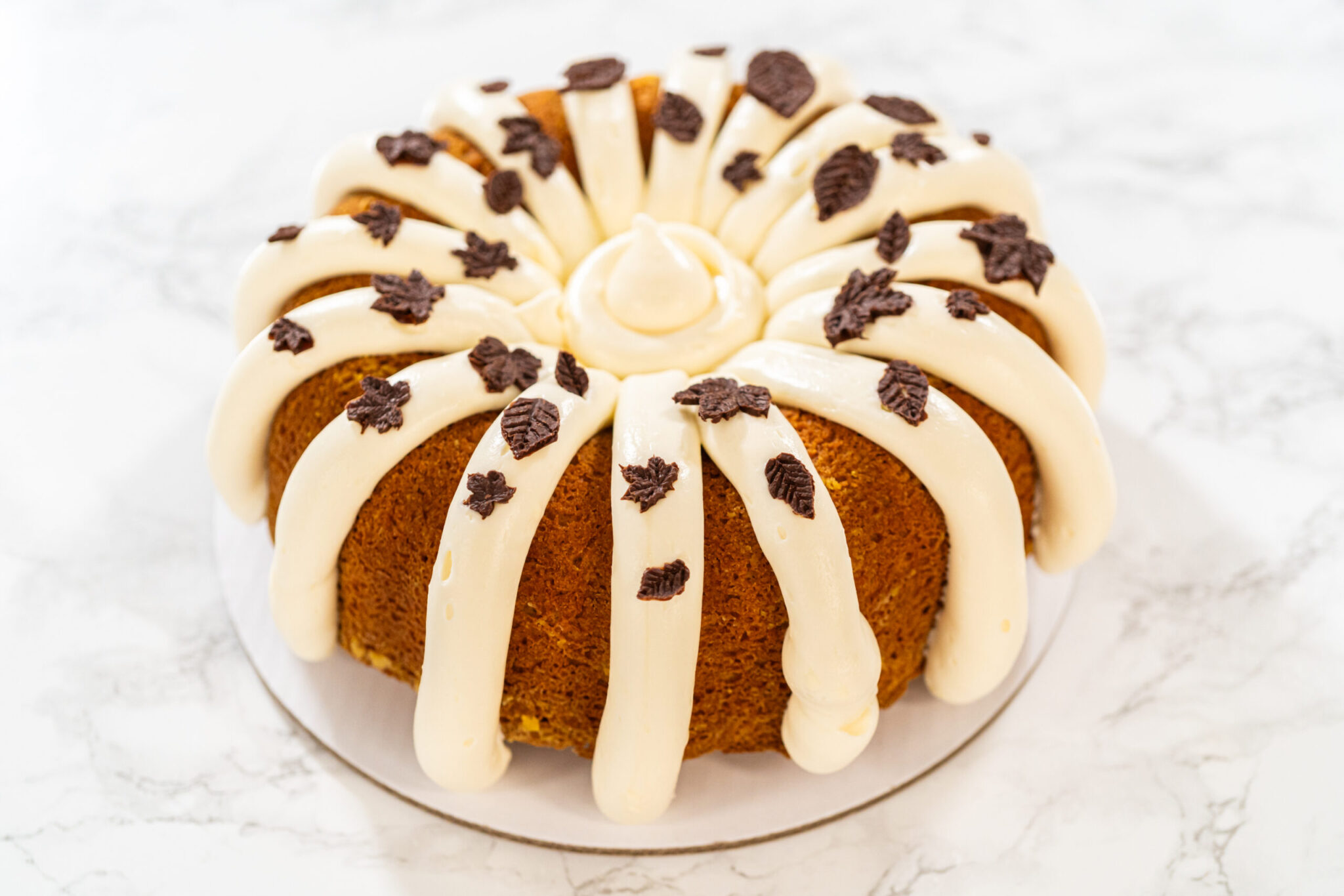 Cream cheese pound cake with frosting and decorative chocolate leaves on a white background.