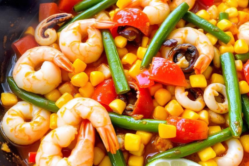 A vibrant dish of shrimp with vegetables, including corn, green beans, cherry tomatoes, and peppers, representing a colorful Mexican seafood stir-fry.