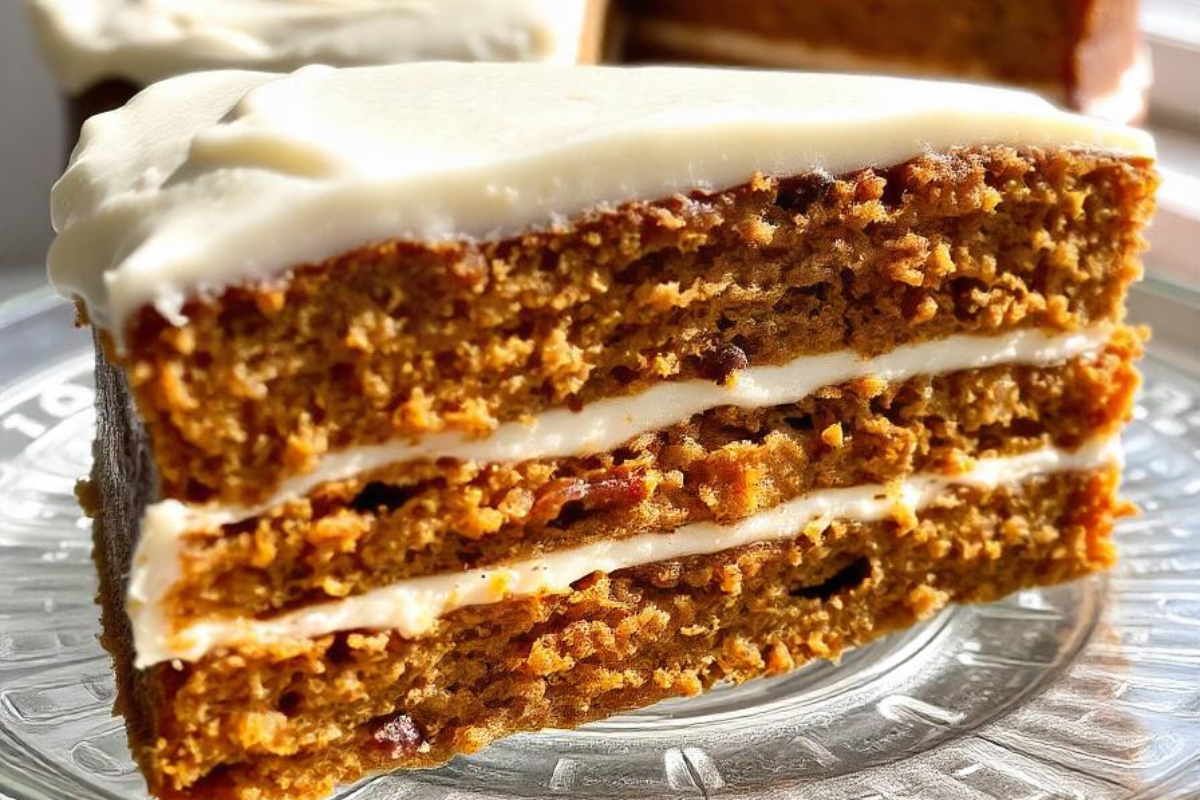 A close-up of a moist carrot cake with three layers of cream cheese frosting, served on a glass plate.