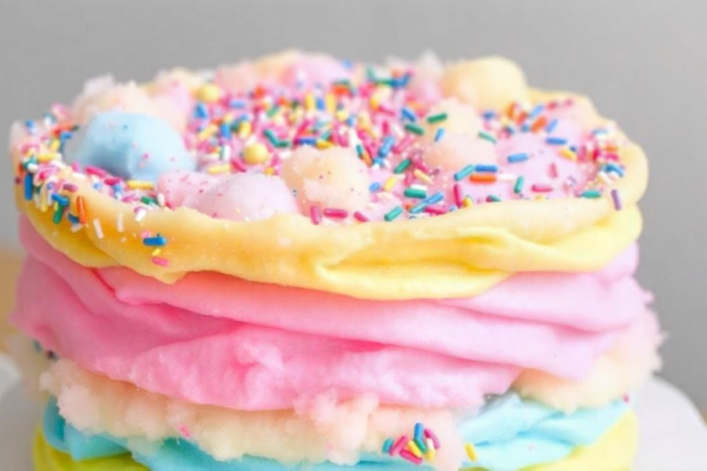 A colorful cotton candy cake with layers of fluffy pink, blue, and yellow cotton candy, arranged on a cake stand.