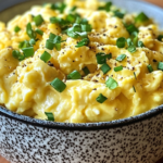 Bowl of fluffy scrambled eggs topped with chopped green onions and seasoned with black pepper.