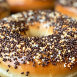 Close-up of a freshly baked scooped bagel topped with seeds and seasoning, resting on a cooling rack.