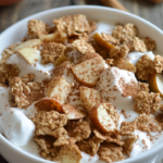 Bowl of apple and cinnamon cereal with yogurt topped with fresh apple slices and sprinkled cinnamon